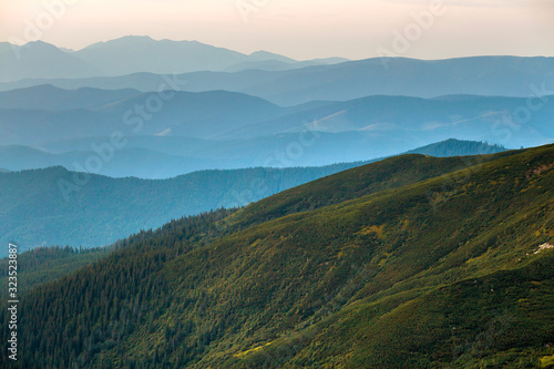 Landscape view of green majestic Carpathian mountains covered with light mist in dawn.