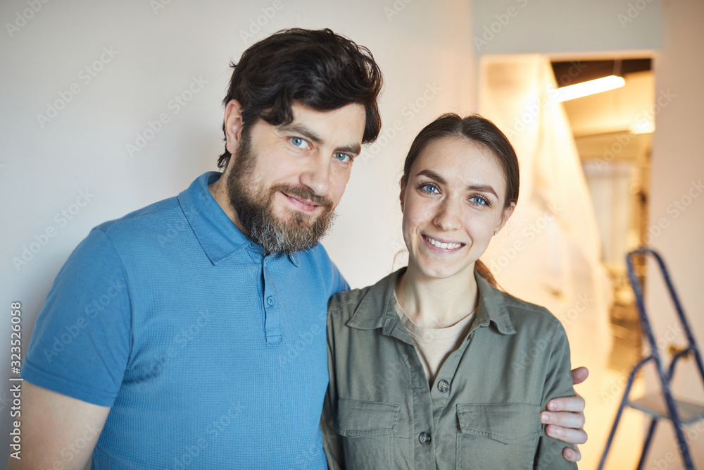 Portrait of happy married couple embracing and looking at camera while renovating house together, copy space Portrait of happy married couple embracing and looking at camera while renovating house together, copy space