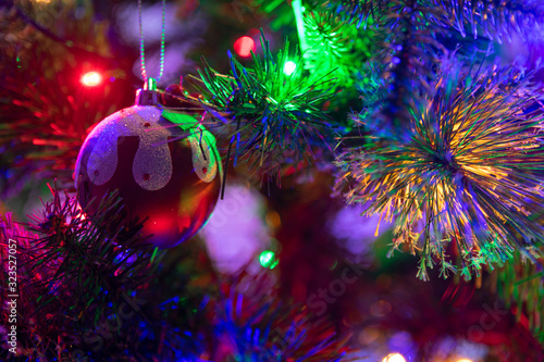 A close up photograph of a Christmas pudding bauble hanging from a green Christmas tree surrounded with multicoloured fairy lights