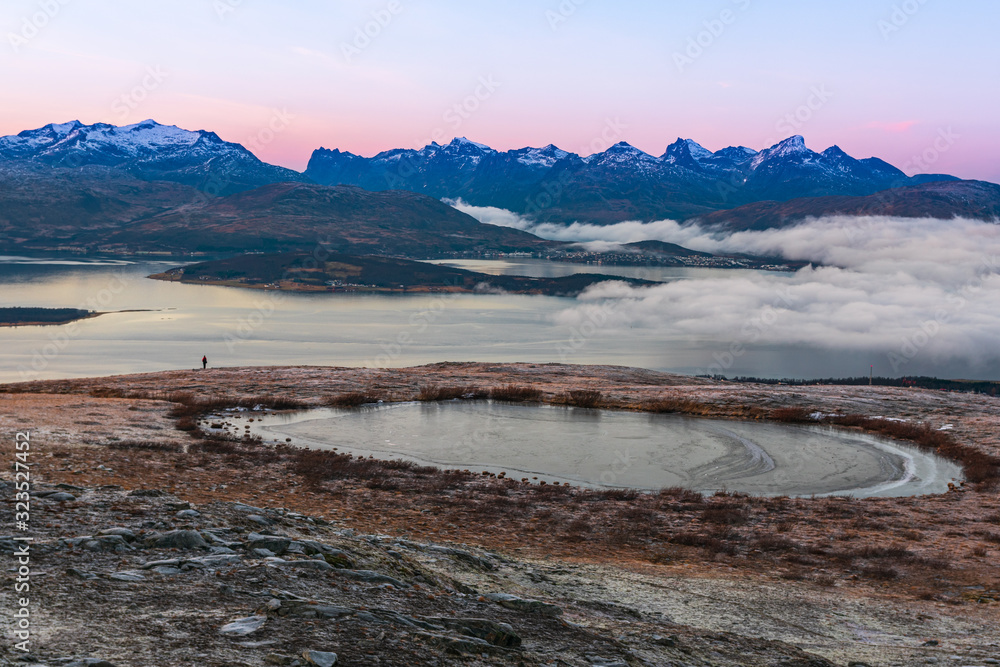 A phtoograph of a large frozen body of water on top of Fløyfjellet in Tromso with a person in the distance