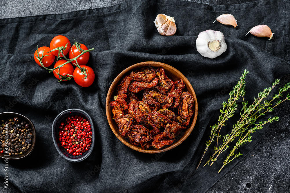 Dried tomatoes with garlic, spices and herbs. Black, dark background. Top view
