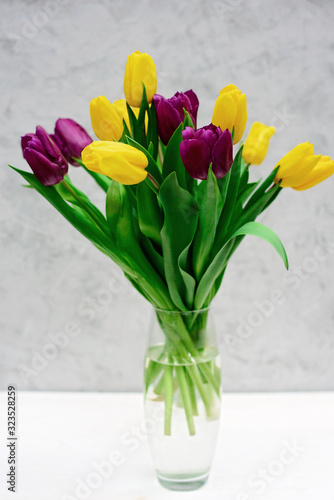 Bouquet of purple and yellow spring tulip flowers in a glass vase on a light background. Mothers Day. International Women's Day.