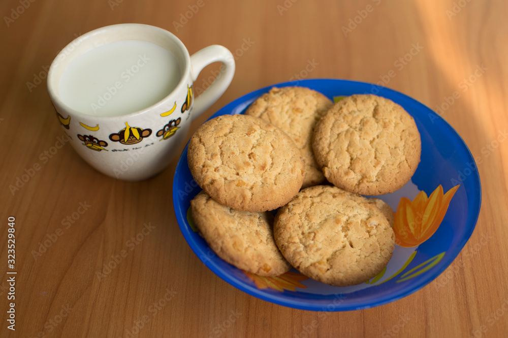 White cup with milk and cookies on wooden background. Homemade oat cookies - a sweet dessert. White cup with milk and cookies on wooden background. Homemade oat cookies - a sweet dessert.
