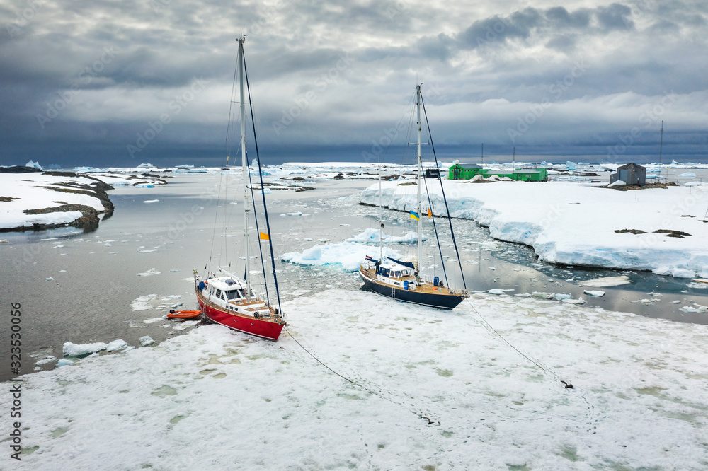aerial view to two yachts staying on ice icebergs and view to buildings of polar station in Antarctica aerial view to two yachts staying on ice icebergs and view to buildings of polar station in Antarctica