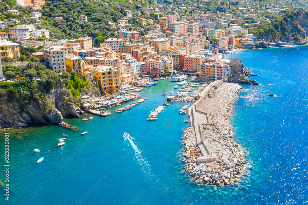 Marina and breakwater where lighthouse is located. Boat sailing to the harbor in ligurian sea, Camogli near Portofino, Italy. Aerial view on traditional Italian colorful houses