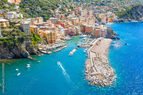 Marina and breakwater where lighthouse is located. Boat sailing to the harbor in ligurian sea, Camogli near Portofino, Italy. Aerial view on traditional Italian colorful houses