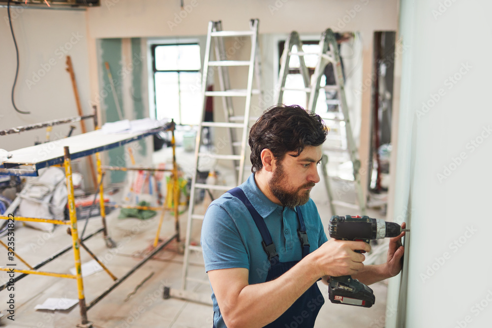 High angle portrait of bearded construction worker drilling wall while renovating house alone, copy space High angle portrait of bearded construction worker drilling wall while renovating house alone, copy space