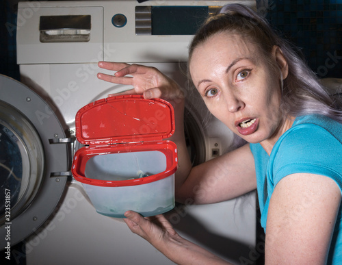 woman in the background of a washing machine peeps in surprise in box with washing gel in her hands, photo from the series