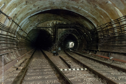 double-track reinforced concrete tunnel of the metro line.One of the railway lines turns of the right.The light is on.Electric high-voltage cables run along the walls of the tunnel   