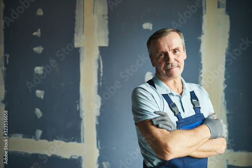 Waist up portrait of senior construction worker smiling at camera while posing confidently against dry wall, copy space photo