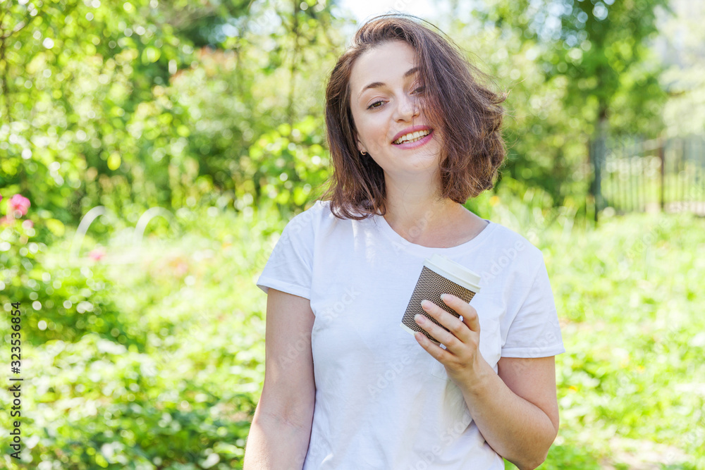 Happy girl smiling outdoor having lunch break. Beautiful young brunete woman with take away coffee cup resting on park or garden green background. Education freelancer resting leisure concept. Happy girl smiling outdoor having lunch break. Beautiful young brunete woman with take away coffee cup resting on park or garden green background. Education freelancer resting leisure concept.