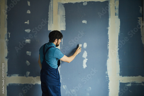Back view portrait of bearded man working on dry wall while renovating house, copy space photo