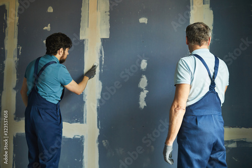 Back view portrait of two construction workers building dry wall while renovating house, copy space photo