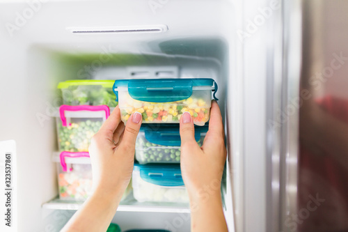 Woman taking container with frozen mixed vegetables from freezer. photo