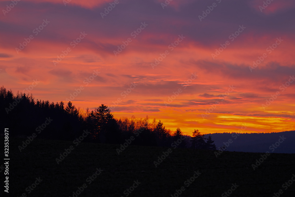 Landscape Picture of the dramatic or romantic red sky clouds over the deep forest or wood during the winter sunset in the highland part of Czech Republic. Beautiful part of country for holliday.