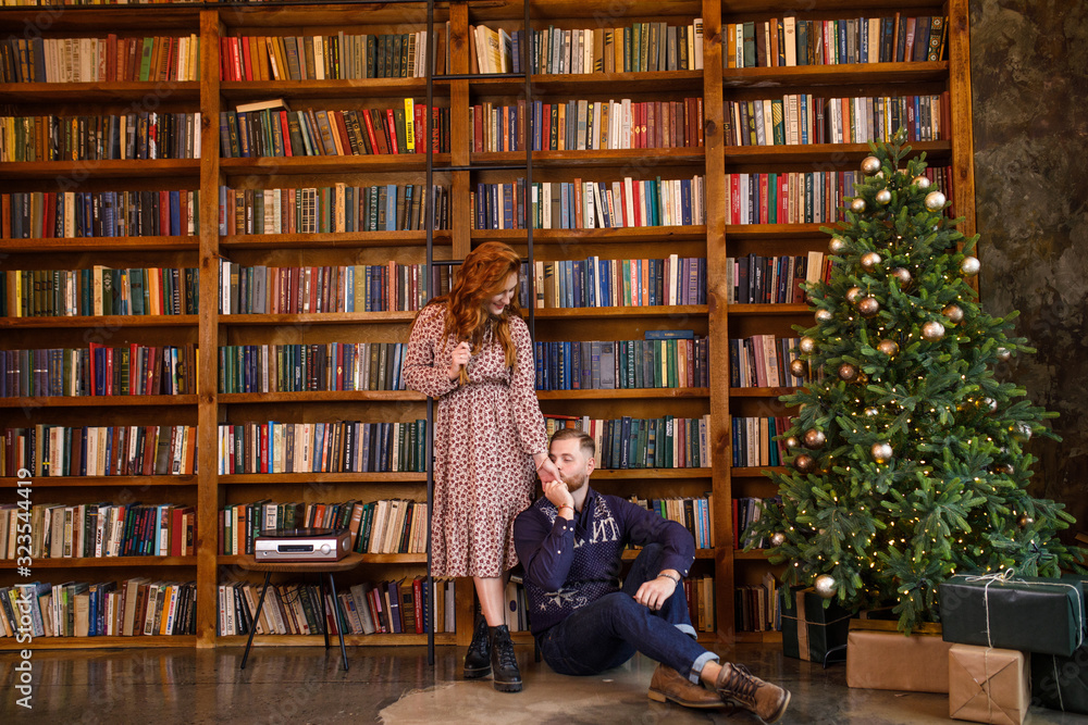 young beautiful couple sitting on the background of the library and books in the apartment in the loft style young beautiful couple sitting on the background of the library and books in the apartment in the loft style