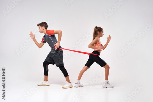 Fitness leaders. Full-length shot of teenage boy and girl engaged in sport, looking focused while exercising using resistance band. Isolated on white background. Training, active lifestyle concept