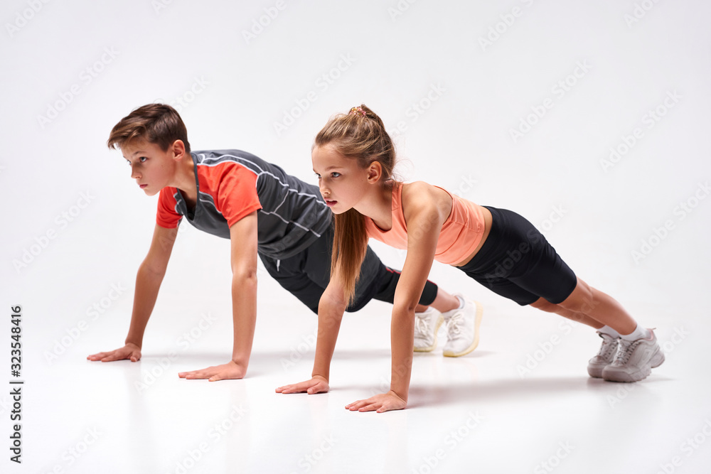 Energizing lives. Full-length shot of teenage boy and girl engaged in sport, looking away while doing push-ups. Isolated on white background. Training, active lifestyle, team concept Energizing lives. Full-length shot of teenage boy and girl engaged in sport, looking away while doing push-ups. Isolated on white background. Training, active lifestyle, team concept