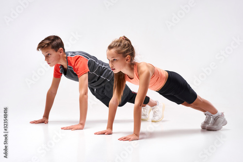 Energizing lives. Full-length shot of teenage boy and girl engaged in sport, looking away while doing push-ups. Isolated on white background. Training, active lifestyle, team concept