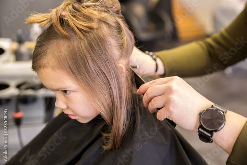 Little girl sitting in hairdresser salon, cover black cape