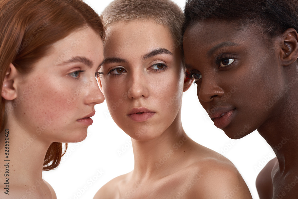 Glowing and healthy skin. Portrait of three multicultural young women standing close to each other in studio against white background. Beautiful models with different skin color standing together Glowing and healthy skin. Portrait of three multicultural young women standing close to each other in studio against white background. Beautiful models with different skin color standing together