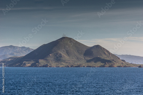 Ensenada, Mexico - January 17, 2012: Dark green mountain with antennas on top behind blue Pacific Ocean under light blue sky at entrance to All Saints Bay.
