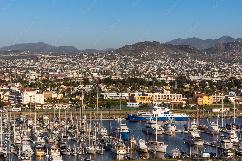 Ensenada, Mexico - January 17, 2012: Yachts and pleasure vessel s moored in the port. Backed by citiscape on hill slope and mountains on horizon under blue sky.