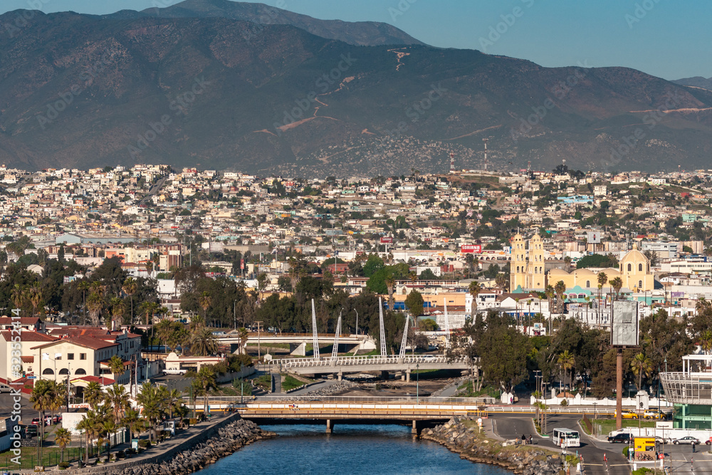 Fototapeta premium Ensenada, Mexico - January 17, 2012: Arroyo Ensenada empties in bay and leads to Yellow Cathedral of Our Lady of Guadalupe under evening sun emersed in cityscape and black moutain as backdrop.