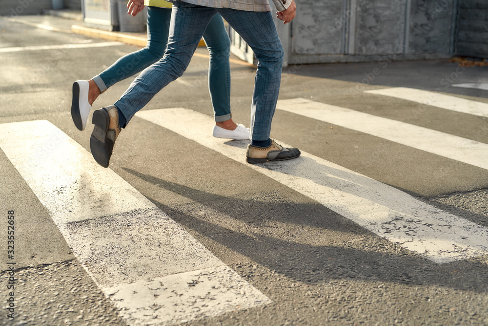 Cropped photo of two people in jeans running across the road. Crosswalk