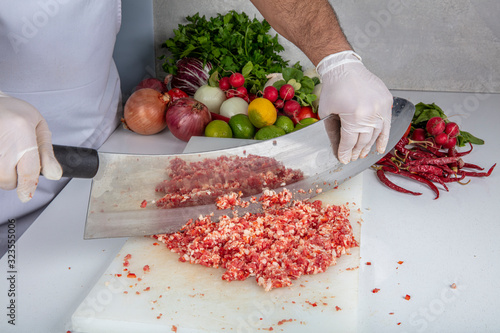 Chef is chopping the raw beef on cutting board with knife to cook in the kitchen, minced beef. Kebab restaurant, kebab preparation. photo