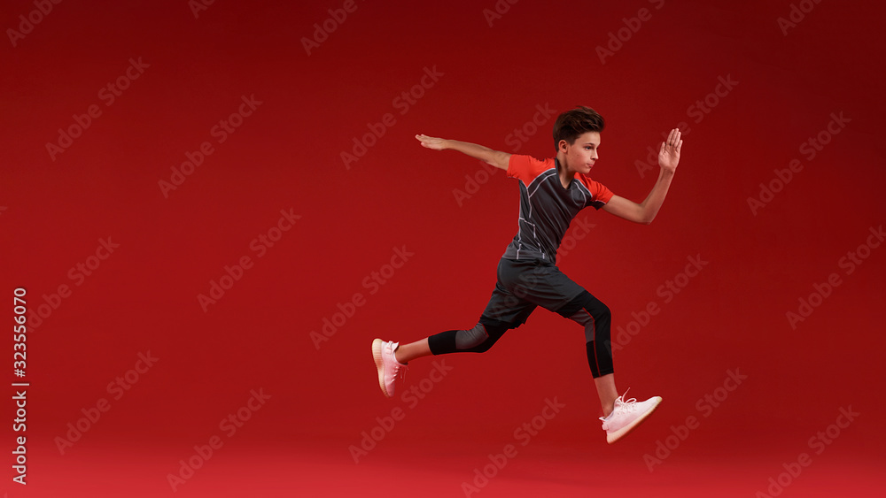Move. A teenage boy is engaged in sport, he is looking away while jumping. Isolated on red background. Fitness, training, active lifestyle concept. Horizontal shot