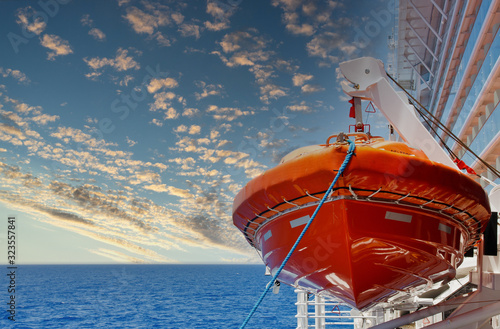 An orange lifeboat hanging over a blue sea on the side of a cruise ship
