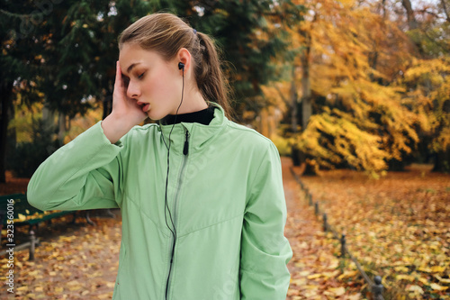 Portrait of tired sporty girl in earphones resting after run in park