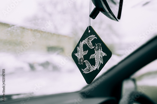 freshener in the car in the form of a drawing of the zodiac sign of a fish on a black square on the background of a snow-covered windshield.