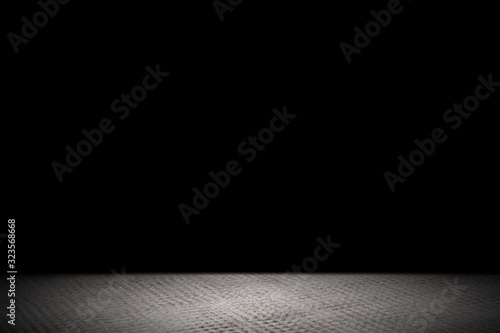 Light shining down on rough gray concrete floor in dark room with copy space, abstract background