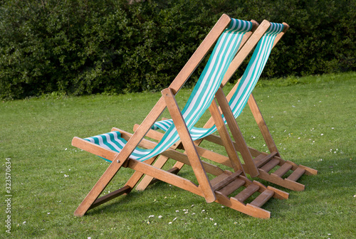 Two empty deck chairs on a lawn of green grass and daisies on a sunny summer day.