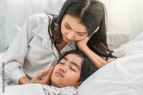 Young Asian mother taking care and checking son Illness on the bed in bedroom house, mom worried high temperature and virus flu, children health care and Contagious disease of corona influenza concept
