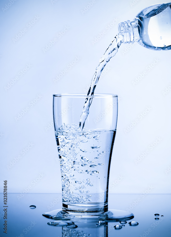 Pouring fresh pure water from bottle into a glass on the table with water drops, Healthcare and beauty hydration concept Pouring fresh pure water from bottle into a glass on the table with water drops, Healthcare and beauty hydration concept