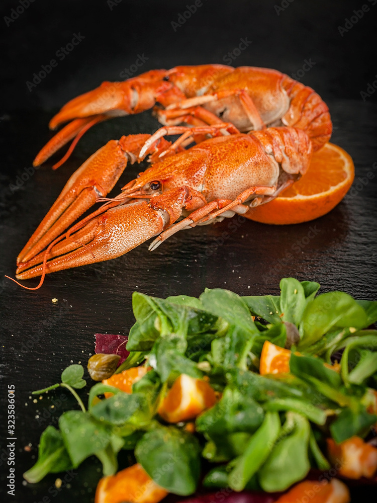 Vertical shot of boiled crawfish and salad with orange and herbs on a cutting board black stone on a dark background. Food porn tasty concept Vertical shot of boiled crawfish and salad with orange and herbs on a cutting board black stone on a dark background. Food porn tasty concept