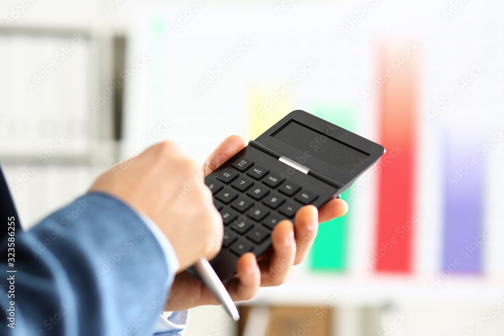 Male arm in suit hold calculator pressing buttons in office closeup. Electronic keypad math data invest credit debit research mortgage loan money saving payment economic debt school