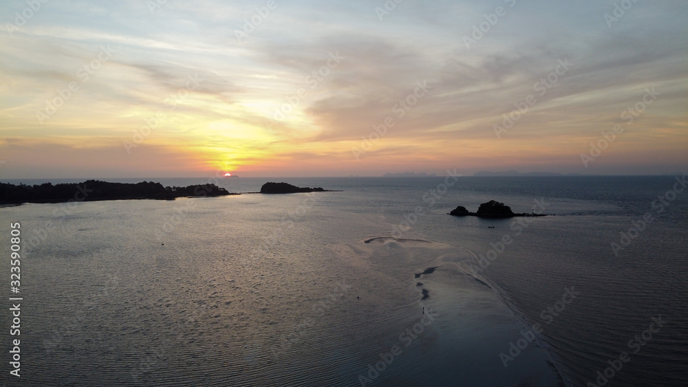 Aerial photo of beautiful sunset view of small island from the beach with small wave and beautiful golden twilight sky.