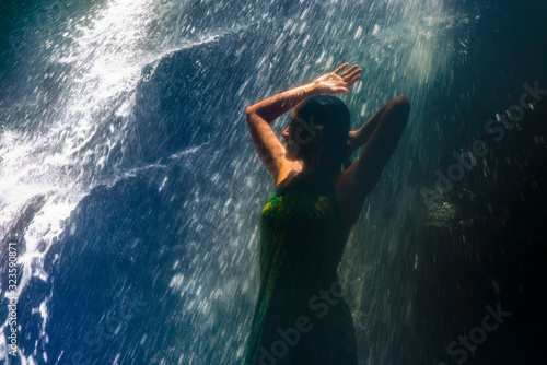 young attractive and blissful Asian Indonesian woman overwhelmed by the beauty and purity of natural waterfall in tropical jungle enjoying happy the amazing and exotic trip