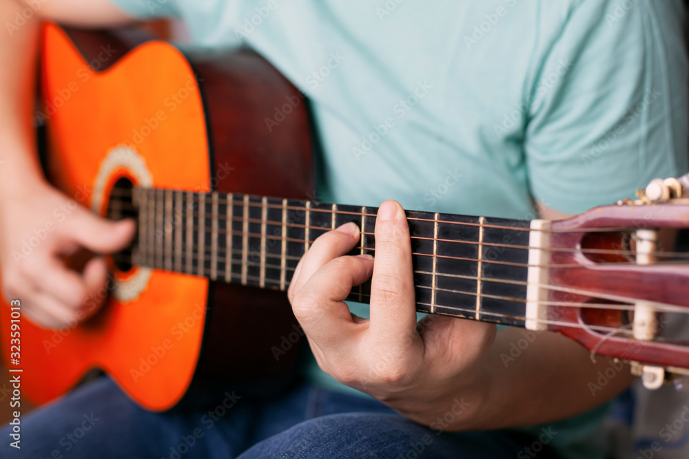 guy plays acoustic guitar, man finger holding a bar chord. learn to play a musical instrument