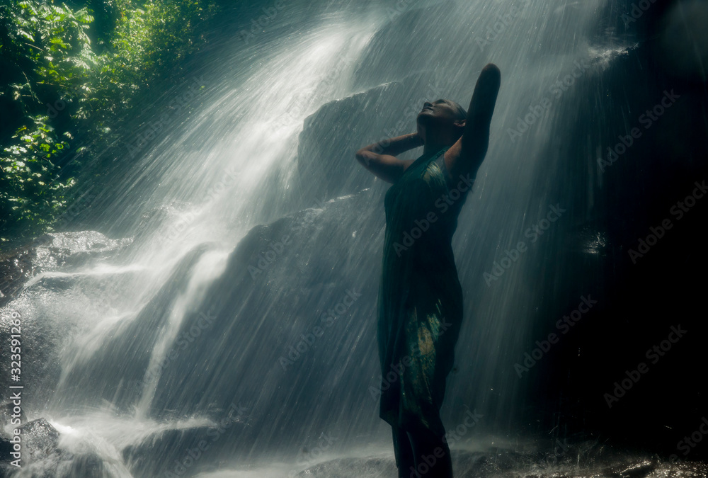Obraz premium young attractive and blissful Asian Indonesian woman overwhelmed by the beauty and purity of natural waterfall in tropical jungle enjoying happy the amazing and exotic trip