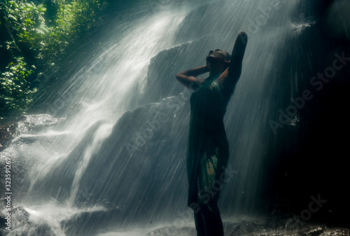 young attractive and blissful Asian Indonesian woman overwhelmed by the beauty and purity of natural waterfall in tropical jungle enjoying happy the amazing and exotic trip