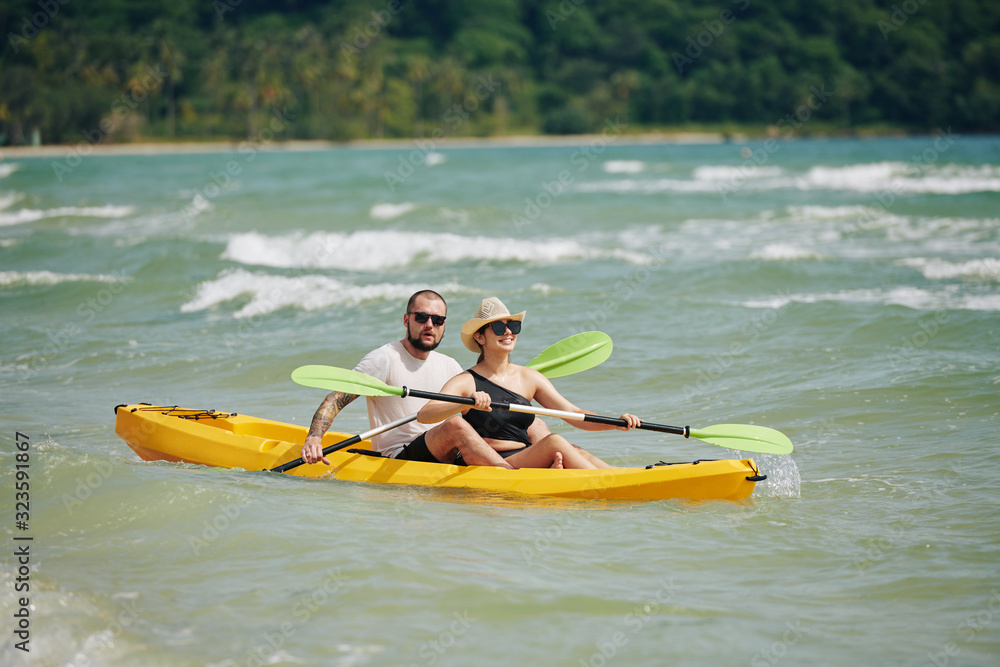 Happy young couple spending weekend together and paddling kayak on lake
