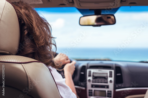 Fototapeta Naklejka Na Ścianę i Meble -  Woman driving a car relaxing in auto trip traveling along ocean tropical beach in background. Traveler concept. Back view