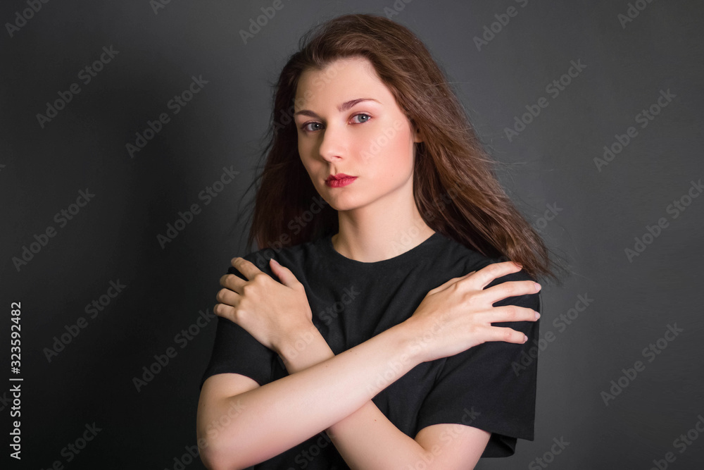 Portrait of a beautiful, young girl in black clothes with long hair. Studio photo, on a gray background. A model with clean skin.