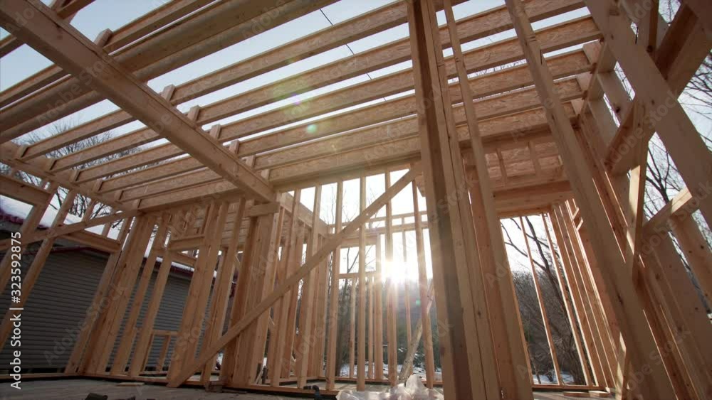 Interior of spacious wooden residential frame house under construction: planks, beams and the bright sun is seen through trussings. Interior of spacious wooden residential frame house under construction: planks, beams and the bright sun is seen through trussings.