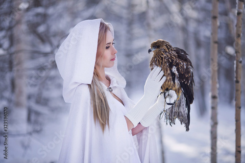 A beautiful girl in a white coat walks in the forest. The huntress with a bird in her hands.